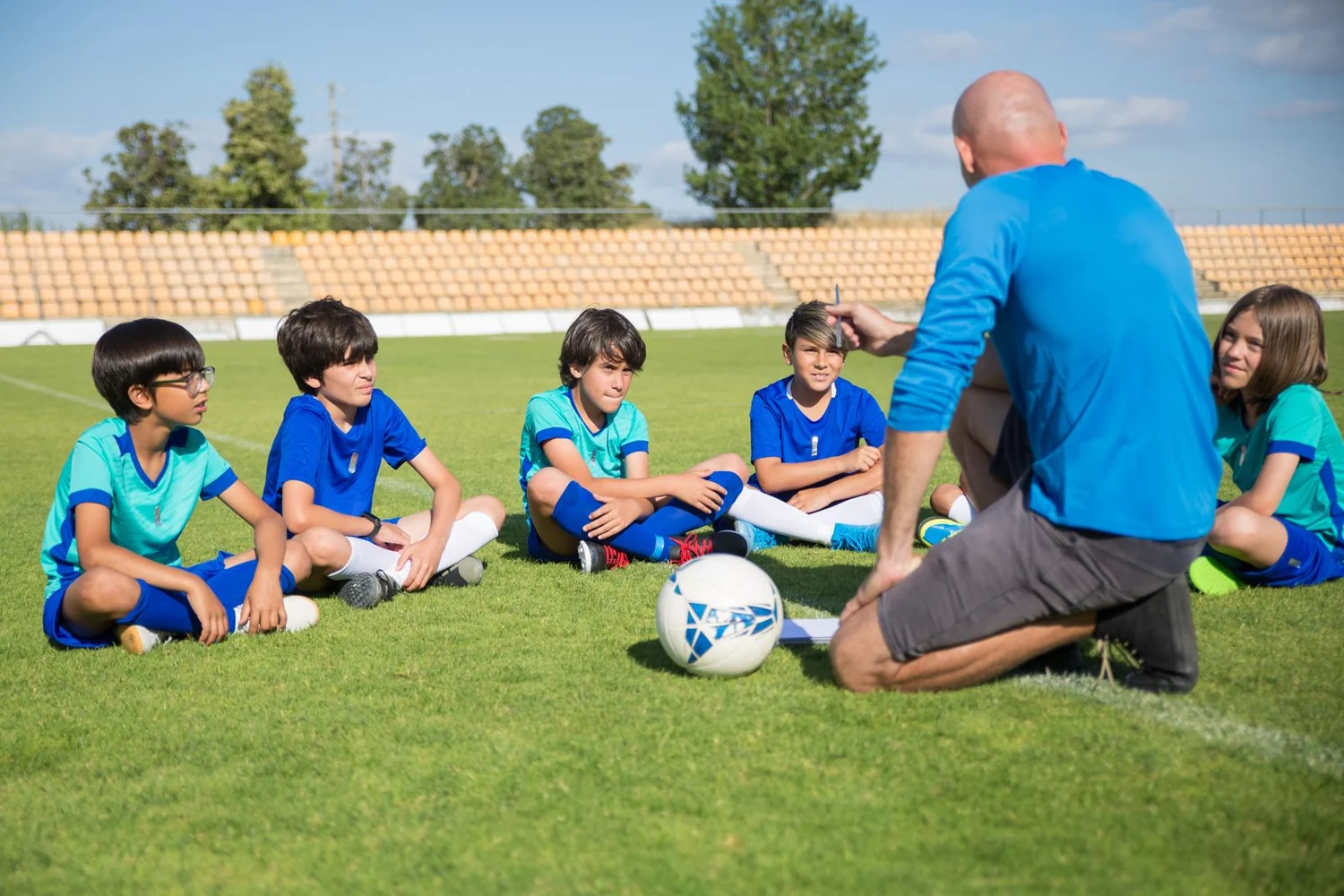 子どもたちと同じ目線の高さで話すサッカーコーチ。写真はイメージです